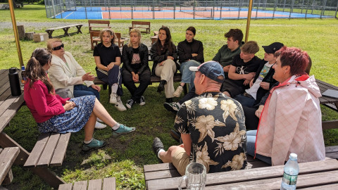 Man sieht verschiende Schüler*innen in einem Kreis sitzend. Eine ältere Frau erzählt.