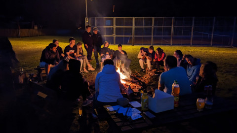 Man sieht verschiendene Menschen um ein Lagerfeuer sitzen.